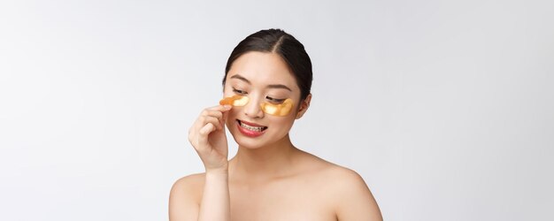 アジアの美しさの10代女性が目の下のゴールドのアイマスクパッチで彼女の肌をケア