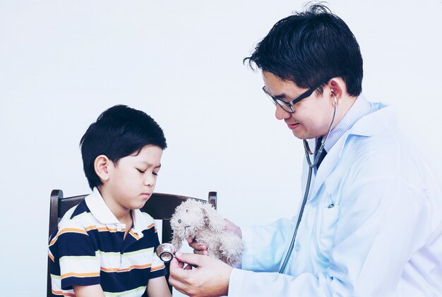 Азиатский мальчик и доктор во время изучения с помощью стетоскопа на белом фоне