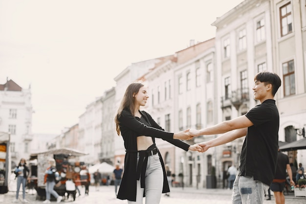 Free photo asian boy and his caucasian girlfriend in casual wear standing on lviv street. couple holding each other hands while walking together in city