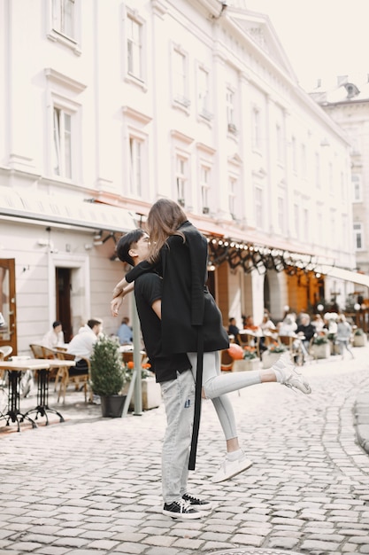 Free photo asian boy and his caucasian girlfriend in casual wear standing on lviv street. couple hugging each other while walking together in city