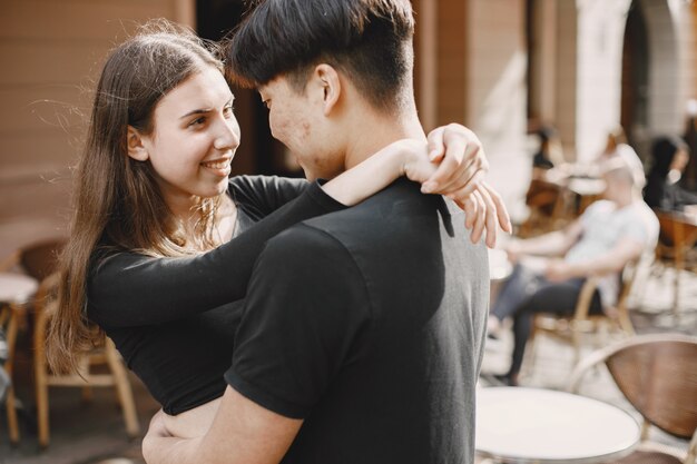 Asian boy and his caucasian girlfriend in casual wear standing on Lviv street. Couple hugging each other while walking together in city