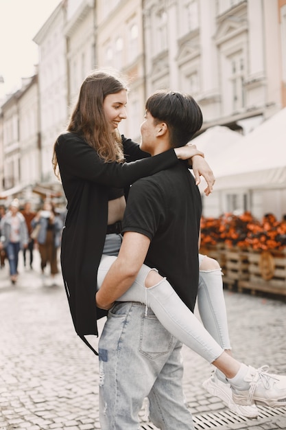 아시아 소년과 그의 백인 여자친구는 평상복을 입고 Lviv 거리에 서 있습니다. 도시를 함께 걷는 동안 서로 포옹하는 커플