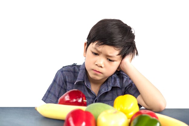 アジアの少年は白い背景の上に嫌いな野菜の表現を見せています。