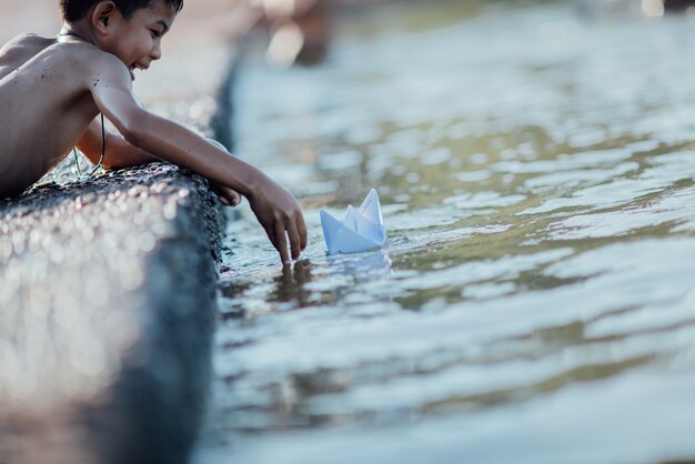 アジアの少年が川で紙の船を遊んで