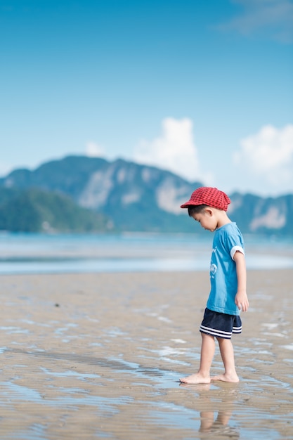 ビーチで歩くアジアの少年海と青空