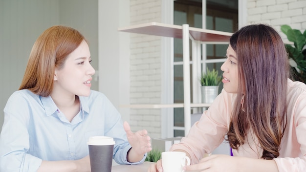 Le donne asiatiche di affari che godono bevendo il caffè caldo, discutono circa lavoro e pettegolezzo chiacchierano di chiacchierata