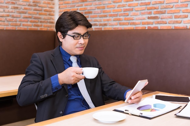 Free photo asian businessman drinking coffee in office looking at phone