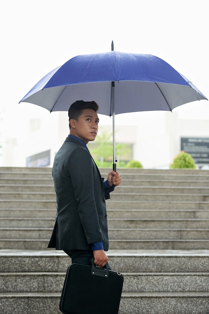 Asian businessman with umbrella and briefcase walking up staircase in rain
