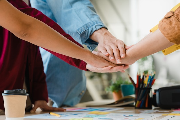 Asian businessmen and businesswomen meeting brainstorming putting hands up for new startup and giving strength motivation working together in modern creative office. Coworker teamwork concept.