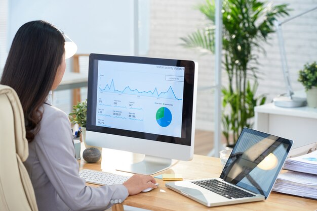 아시아 사업가 사무실에서 책상에 앉아 큰 컴퓨터 화면에서 그래프를 공부