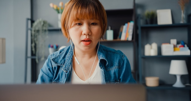 asian businesswoman using laptop talk to colleagues about plan in video call while working from house at living room