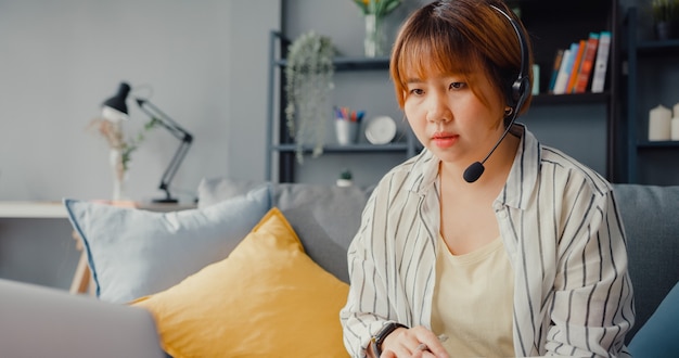 Free photo asian businesswoman using laptop talk to colleagues about plan in video call while working from house at living room