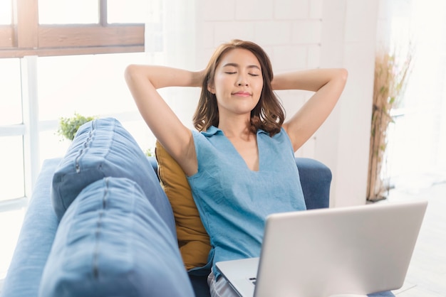 Asian businesswoman using laptop work at home stretch relax breathe fresh air on sofa. social distancing concept.