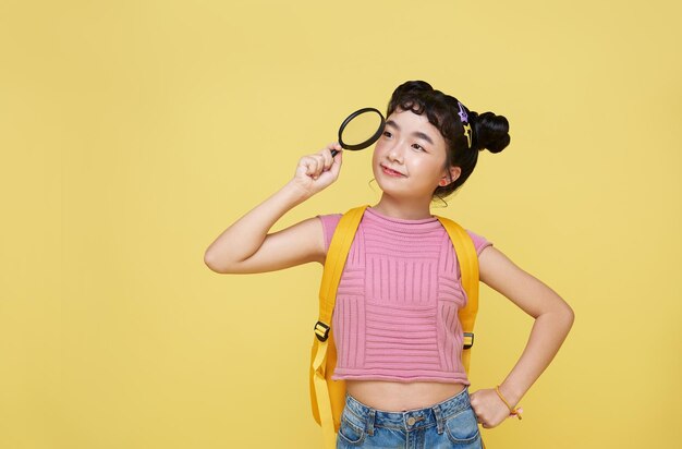 Asian child schoolgirl stood in casual wear looking at camera through magnifier