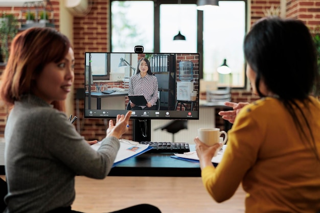 Asian colleagues collaborating with remote employment discussing cv resume during online videocall meeting conference. Teleconference call on computer screen in startup business office