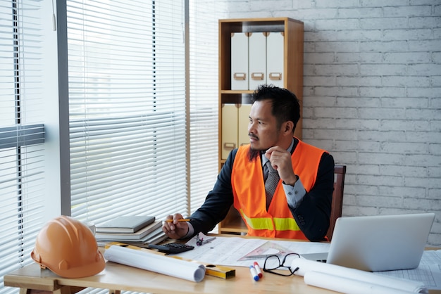 Free photo asian construction firm executive in business suit and safety vest sitting in office