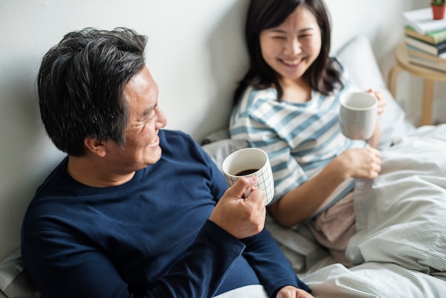 Asian couple drinking coffee in bed