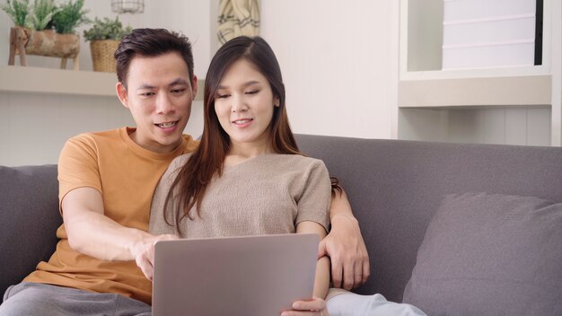 집에서 거실에서 검색 웹에 노트북을 사용하는 아시아 부부