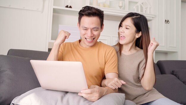 집에서 거실에서 검색 웹에 노트북을 사용하는 아시아 부부