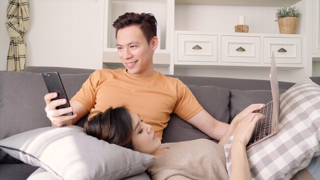 Asian couple using smartphone and laptop checking social media in living room at home