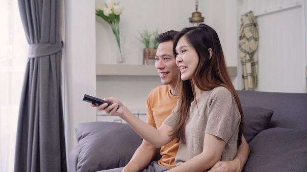 Asian couple watching TV and drinking warm cup of coffee in living room at home, sweet couple enjoy 