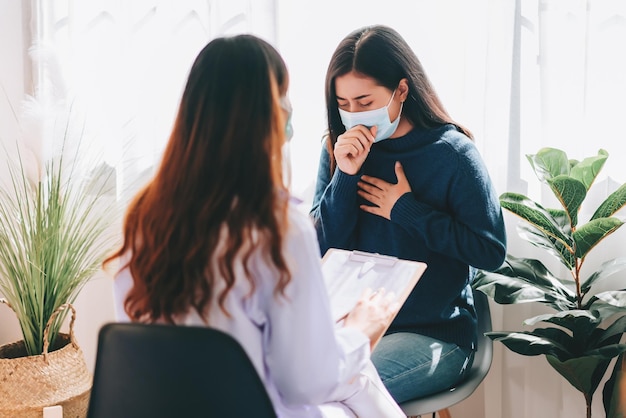 아시아 의사는 기침과 독감 증상이 있는 병원에 있는 젊은 성인 여성을 방문하여 검사합니다.