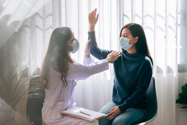 Asian doctor visit and examines on young adult woman at hospital with office syndrome symptomThe doctor checking up and consulting for health care wearing a mask to protect covid19 pandemic