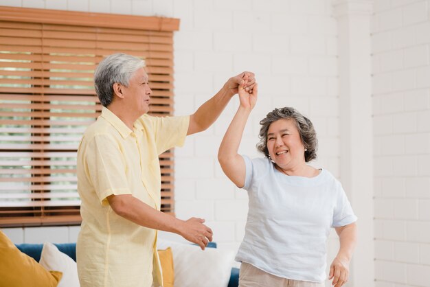 Азиатские пожилые пары танцуют вместе, в то время как слушают музыку в гостиной дома, сладкие пары наслаждаются моментом любви, весело проводя время, когда они расслаблены дома.