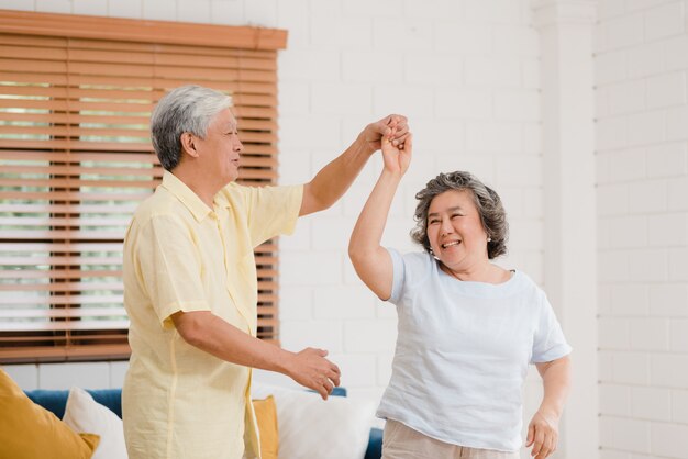 Asian elderly couple dancing together while listen to music in living room at home, sweet couple enjoy love moment while having fun when relaxed at home. 