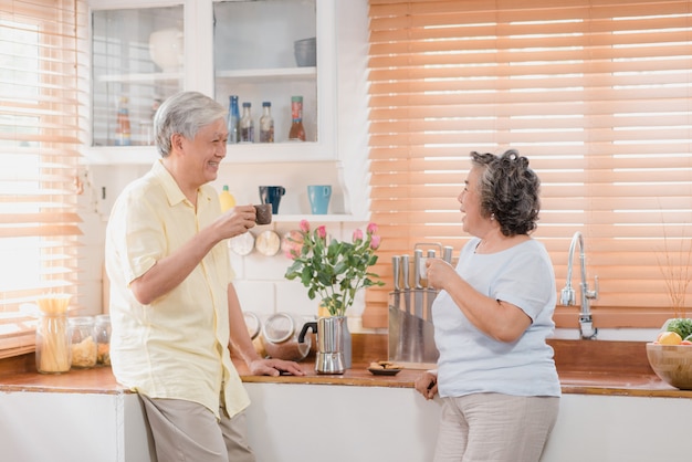 Asian elderly couple drinking warm coffee and talking together in kitchen at home. 