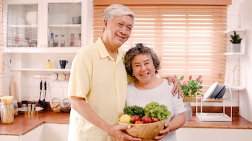 Asian elderly couple feeling happy smiling and holding fruit and looking to camera while relax in kitchen at home. lifestyle senior family enjoy time at home concept.