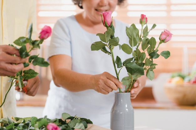 アジアの老夫婦が自宅の台所で木製のテーブルの上に花束の花を作る。