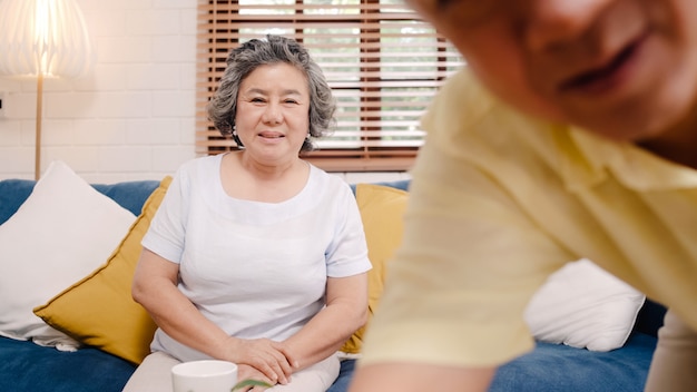 무료 사진 집에서 거실에 소파에 누워있는 동안 손자와 스마트 폰 화상 회의를 사용하여 아시아 노인 부부.