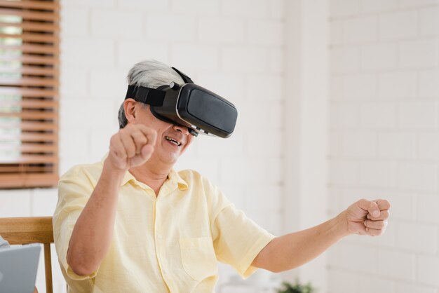 タブレットと仮想現実シミュレータを使用してリビングルームでゲームをしているアジアの老夫婦