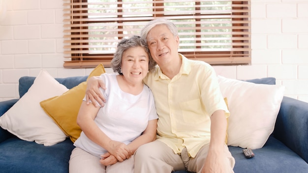 Asian elderly couple watching television in living room at home, sweet couple enjoy love moment while lying on the sofa when relaxed at home. 