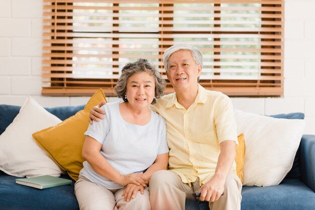 Asian elderly couple watching television in living room at home, sweet couple enjoy love moment while lying on the sofa when relaxed at home.