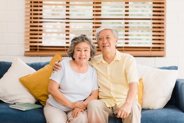 Asian elderly couple watching television in living room at home, sweet couple enjoy love moment while lying on the sofa when relaxed at home. 