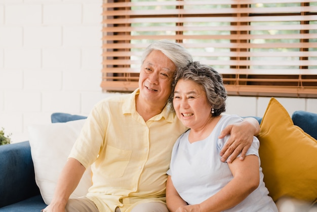Asian elderly couple watching television in living room at home, sweet couple enjoy love moment while lying on the sofa when relaxed at home. 