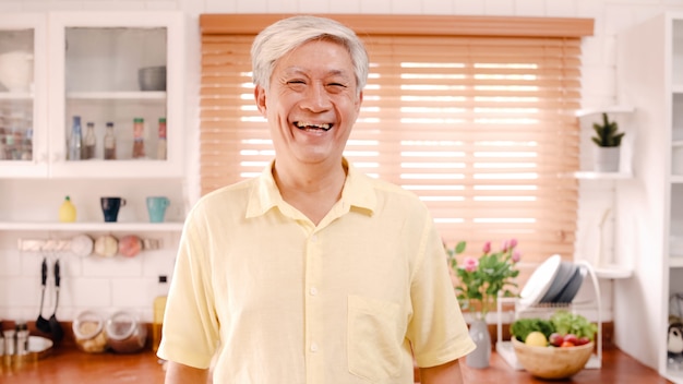 無料写真 アジアの老人が幸せな笑みを浮かべて、自宅のキッチンでリラックスしながらカメラを探しています。
