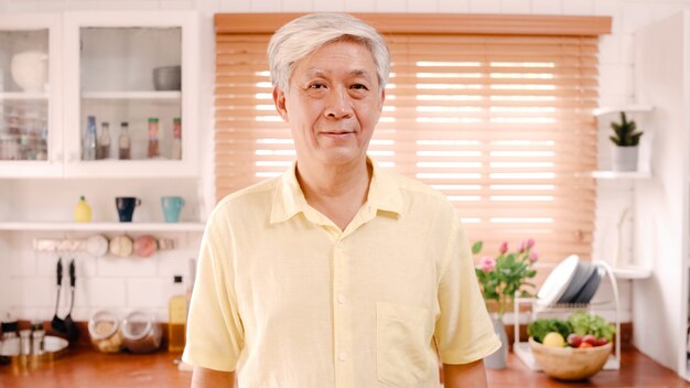 アジアの老人が幸せな笑みを浮かべて、自宅のキッチンでリラックスしながらカメラを探しています。