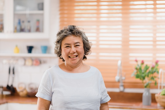 Asian elderly woman feeling happy smiling and looking to camera while relax in kitchen at home.