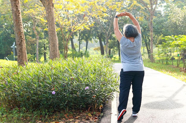 朝、公園でジョギングしているアジアの年配の女性は、健康な体を幸せにしています。高齢者が健康であるためのヘルスケアの概念。コピースペース