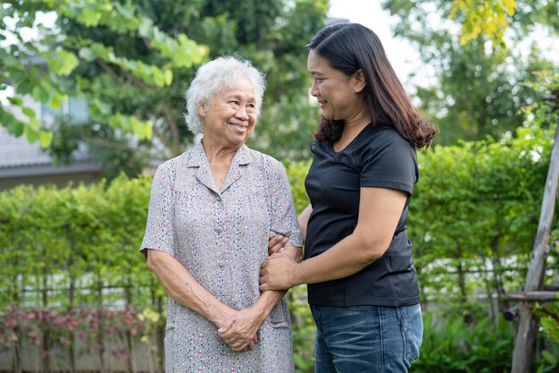 介護者と一緒にアジアの年配の女性は、自然公園で歩いて幸せに抱きしめます。