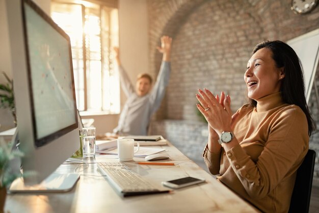 사무실에서 컴퓨터를 사용하면서 비즈니스 성공을 축하하는 아시아 기업가와 그녀의 동료