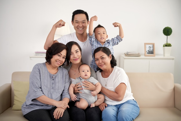 Asian extended family with baby and toddler posing together around couch at home