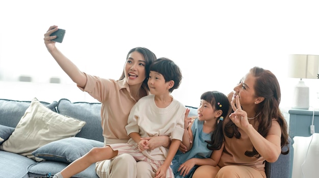 リビングルームで一緒に自分撮り写真を撮るスマートフォンを使用して幸せなアジアの家族