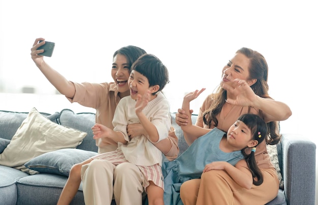 リビングルームで一緒に自分撮り写真を撮るスマートフォンを使用して幸せなアジアの家族