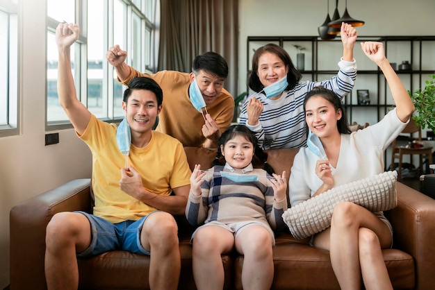 Asian family strong together against covid virus epidemic spreadasian multi generation family with face mask cheering hand rise up show how strong healthy they havefamily smile with confident home