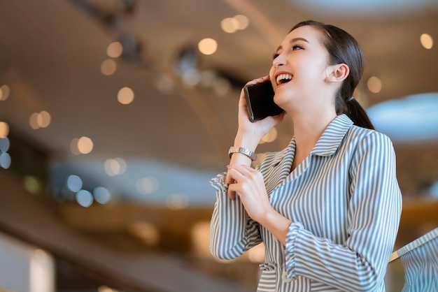 아시아 여성 비즈니스 소유자는 스마트폰 및 노트북 비즈니스 기술과 흐릿한 백화점 보케 배경을 통해 손으로 통신합니다.
