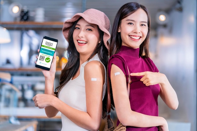 아시아 여성의 쾌활한 미소 짓는 10대 손 제스처 포인트는 코로나19에 대한 백신 브랜드와 백신을 맞은 후 스마트폰 화면에서 디지털 백신 여권을 보여 건강 개념을 예방합니다.